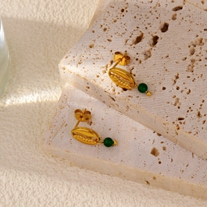 Macro detail of 18k gold conch-shaped earrings with hanging deep green gemstone beads
