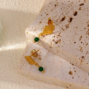 Dettaglio degli orecchini a rombo dorati con perla verde smeraldo e trama martellata