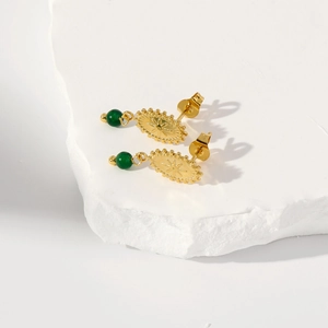Vista macro de pendientes de sol vintage en oro 18k con esmeralda sobre piedra blanca