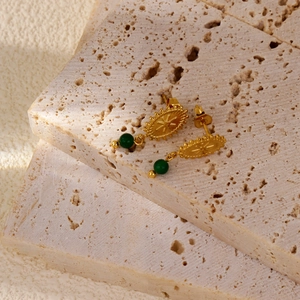 Detalle de pendientes vintage bañados en oro 18k con diseño de sol y cuentas verde esmeralda