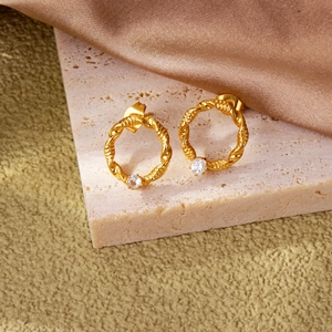 Λεπτομέρεια από στριφτούς κρίκους 18k με ζιργκόν πάνω σε πέτρινη επιφάνεια