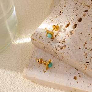 Detail of four-pointed star stud earrings with turquoise stones on travertine stones