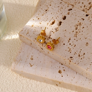 Detailed close-up of 18k gold flower earrings with crystals on a travertine background