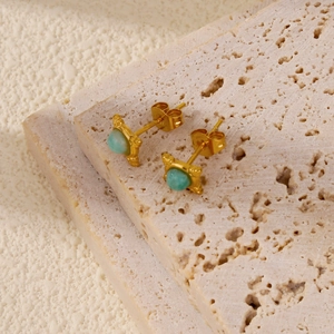 Detailed close-up of gold stud earrings featuring round green gemstones on a stone surface