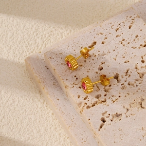 Macro shot of 18k gold floral earrings with pink zircon stone on a stone surface