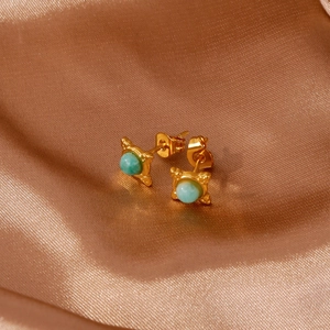Detailed close-up of emerald clover earrings on champagne silk background