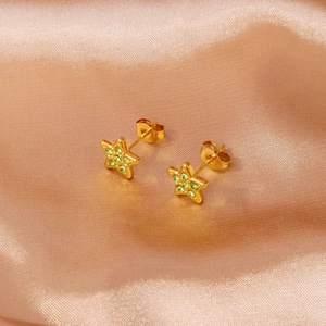 Makroaufnahme goldener Sternohrringe mit grünen Kristallen auf Champagner-Satin