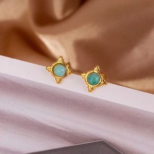 Macro shot of gold star studs with green emerald inlay and vintage sunburst texture