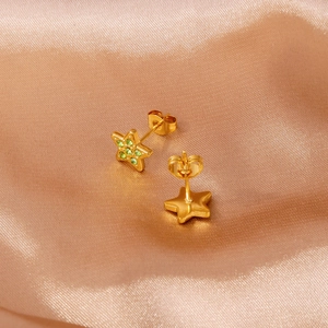 Detail von sternförmigen Goldohrringen mit grünen Steinen auf weicher Seide