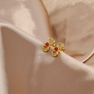 Close-up of 18k gold infinity bow earrings with inlaid red gemstones on silk fabric