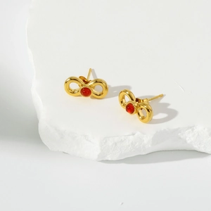 Detailed shot of golden bow earrings with red gemstone on a white marble display