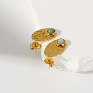Detailed macro view of gold oval earrings with hammered texture and green gemstones