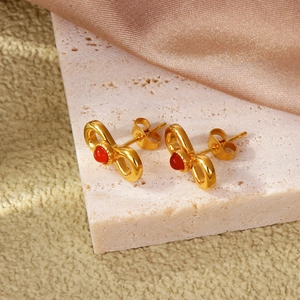 18k gold plated stainless steel bow earrings featuring inlaid red gemstones on stone stand