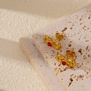 Macro shot of gold-plated bow earrings with red ruby inlay on a textured stone