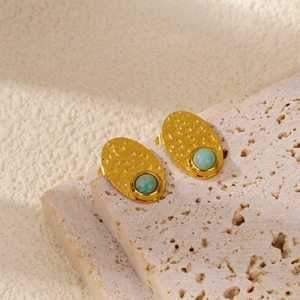 Detail of vintage gold earrings with lava texture and inlaid green gemstones on stone