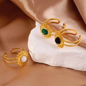 Detail of three sunflower rings with green, black and white stones on champagne silk
