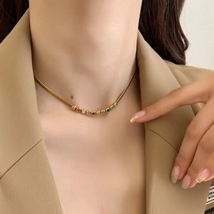 Golden snake chain necklace with rainbow zircon gemstones worn by a model in a suit