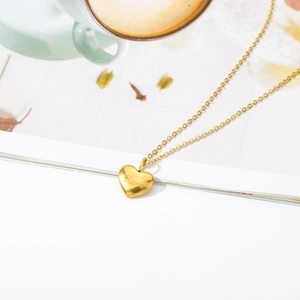 18K gold heart pendant necklace with Love engraving on a minimalist magazine background