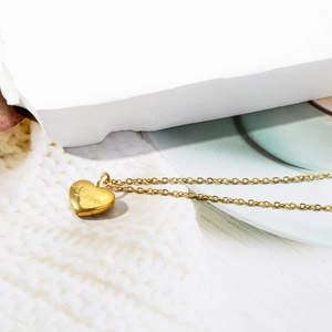 Polished 18K gold heart pendant necklace with Love engraving on a white knit background
