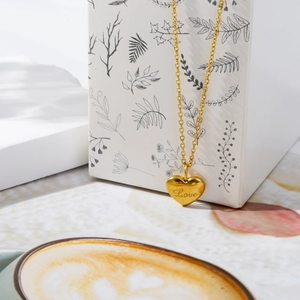Detail of a gold heart pendant necklace with Love engraving on a gift box background