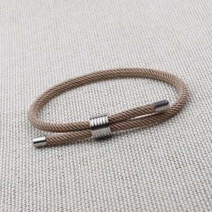 Detail view of khaki woven rope bracelet with silver sliding metal charms and toggle ends