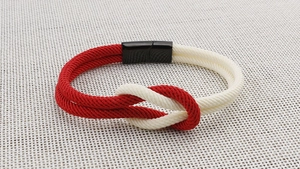 Detail eines rot-weiß geflochtenen Seilarmbands mit Magnetverschluss auf Texturfläche