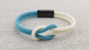 Detail eines blau-weiß geflochtenen Seilarmbands mit schwarzem Magnetverschluss und Segelknoten