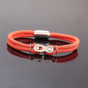 Bracelet chaîne tressé orange avec fermoir magnétique sur surface noire réfléchissante