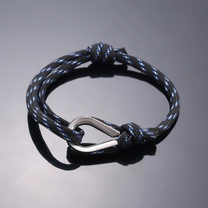 Detail of woven fiber bracelet with polished silver horseshoe clasp on reflective surface