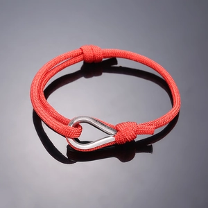 Close-up of red braided rope bracelet with a silver U-shaped metal buckle on a dark background