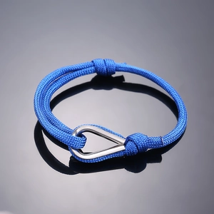 Detail of blue braided rope bracelet with polished silver teardrop metal clasp on dark glass