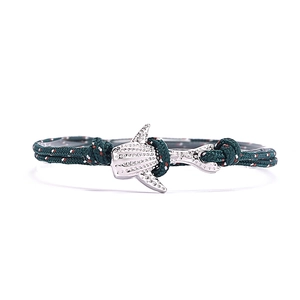 Gros plan d'un bracelet en corde tressée vert foncé avec un pendentif requin-baleine argenté