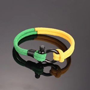 Detail van groen en geel gevlochten armband met een zwarte metalen D-sluiting