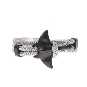 Detail of grey braided cord bracelet featuring a matte black manta ray anchor charm