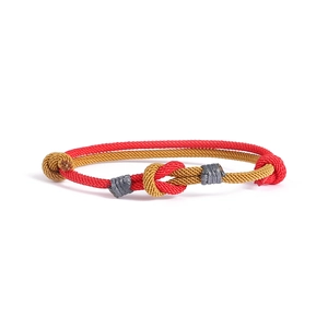 Dettaglio di braccialetti intrecciati a mano in rosso e oro con nodi a incastro fini