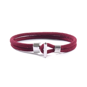 Detail of red braided rope bracelet featuring a polished silver T-bar clasp and metal rings