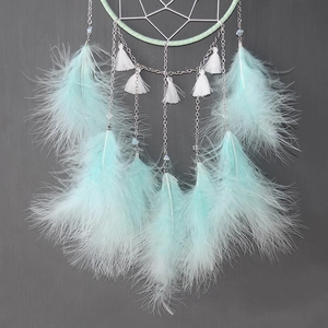 Detail of mint green feathers and white cotton tassels on a handmade moon dream catcher