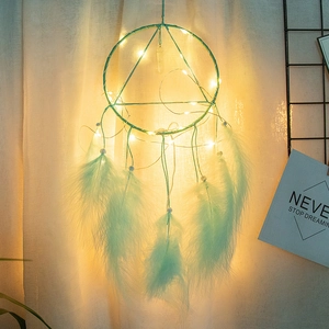 Detail of mint green dream catcher with LED string lights and feathers hanging on wall