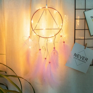 Macro detail of a light-up dream catcher with pink feathers and warm LED string lights