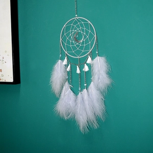 Close-up of white feather dream catcher with a crescent moon pendant on teal background