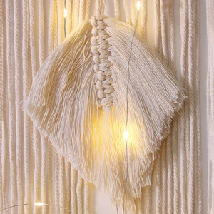 Detailed close-up of ivory macrame feather wall hanging with warm glowing fairy lights