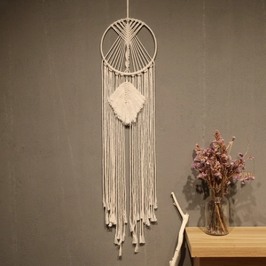 Detail of bohemian woven cotton dreamcatcher with leaf shape and long tassels on gray wall