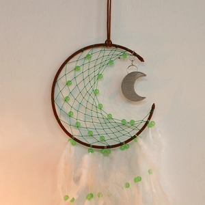 Detail of moon dreamcatcher with green woven net, white feathers and silver moon pendant