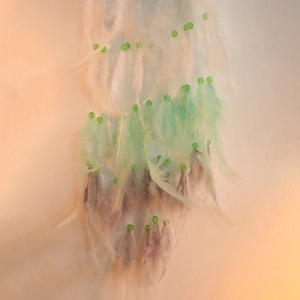 Close-up of handmade moon dream catcher featuring green feathers and decorative beads