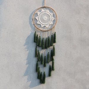 Detail of dark green tassels and crochet mandala dreamcatcher on a textured wall
