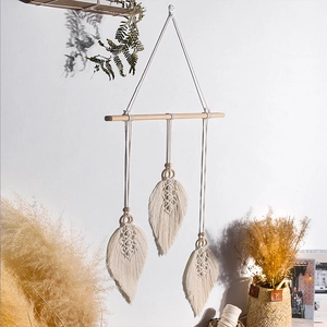 Detail of three handmade bohemian cotton woven leaves hanging on a wooden rod with beads