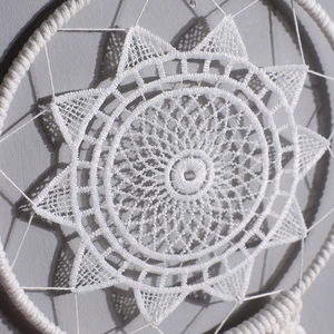 Close-up of hand-woven white macrame dreamcatcher with intricate lace sunburst pattern