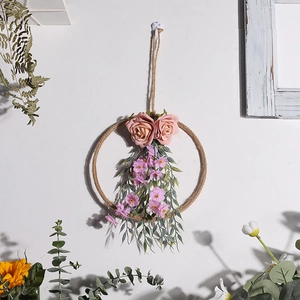 Dettaglio di ghirlanda in canapa con rose rosa e fiori viola su una parete bianca