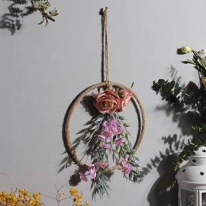 Dettaglio di una ghirlanda in corda con rose rosa e foglie verdi su una parete bianca