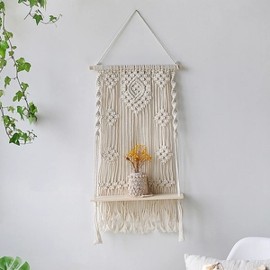 Detail of bohemian hand-woven cotton macrame wall hanging with natural wood shelf